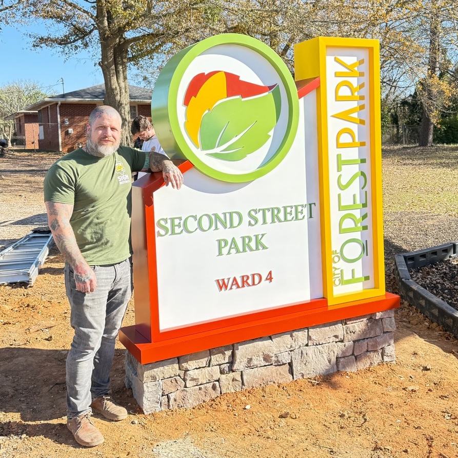 Person stands outdoors, near grass, rocks, and trees